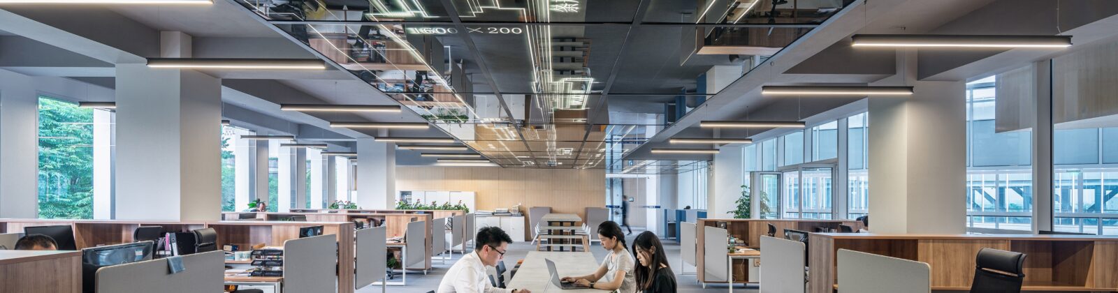 Three people at a desk in a large open office space